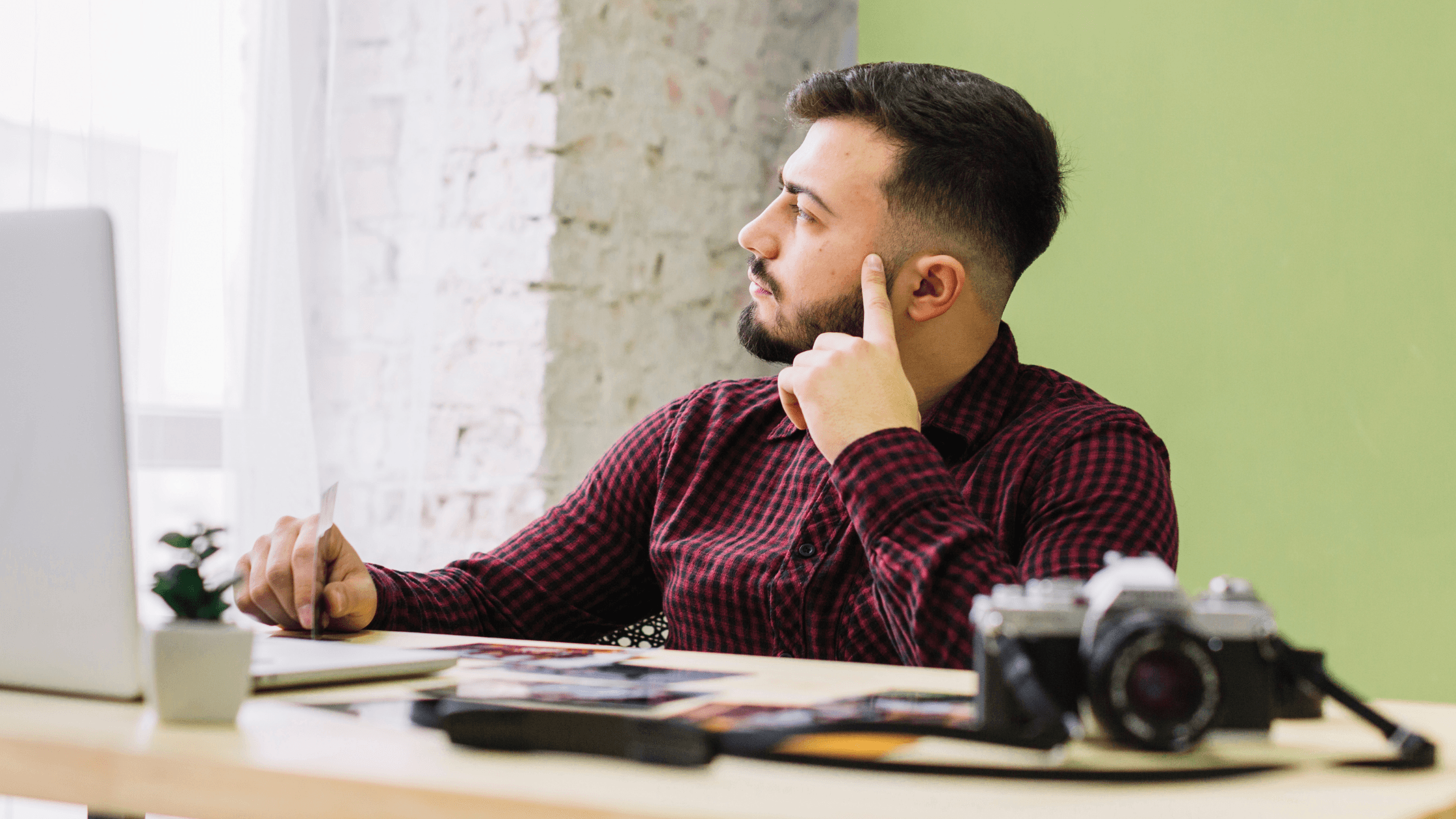 Content creator sitting at a desk with a computer and camera, thoughtfully reviewing work while planning business and tax decisions.